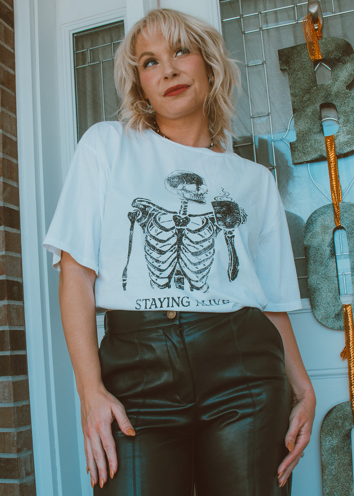 Person wearing a white t-shirt with a skeleton design and text, standing in front of a door.