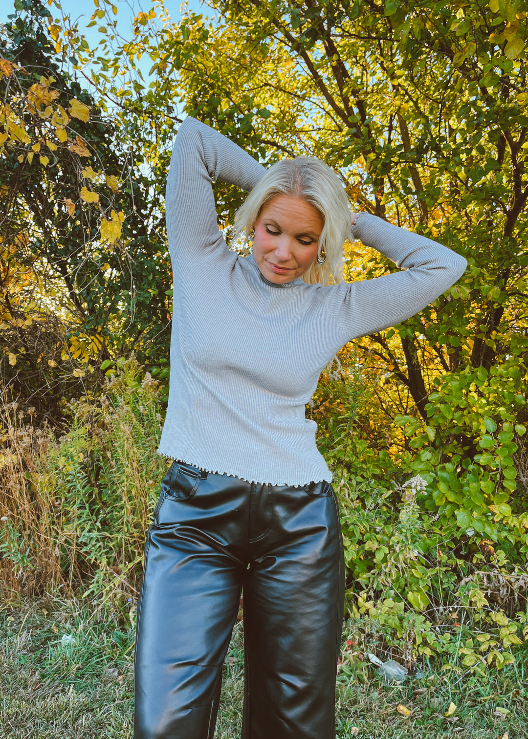 Person wearing a light gray long sleeve top and black pants in a forest setting