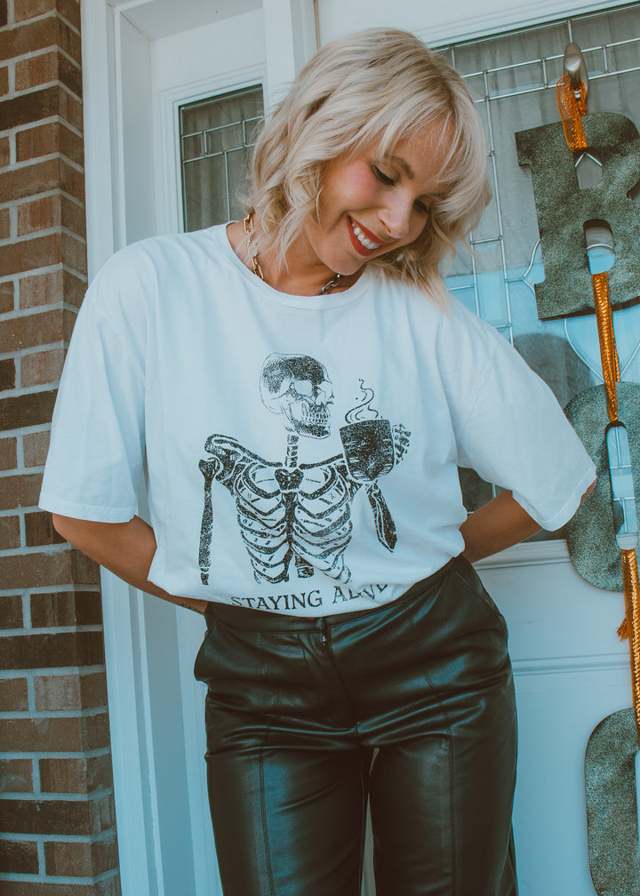 Person wearing a white t-shirt with a skeleton graphic and text, standing in front of a door.