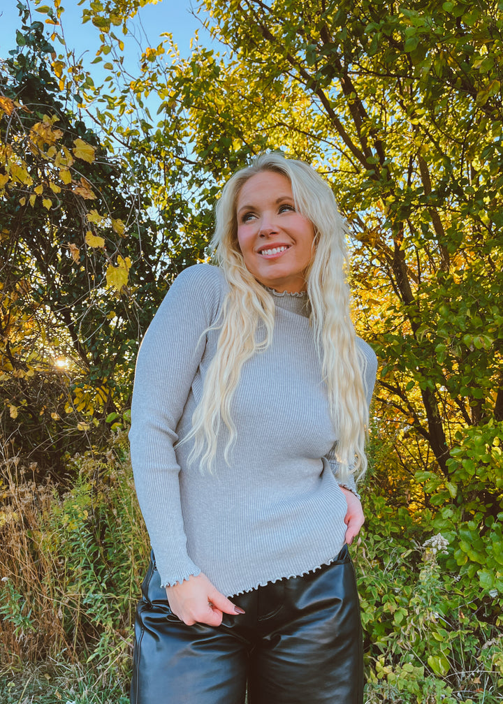 Woman in a gray top standing in a forest with autumn foliage
