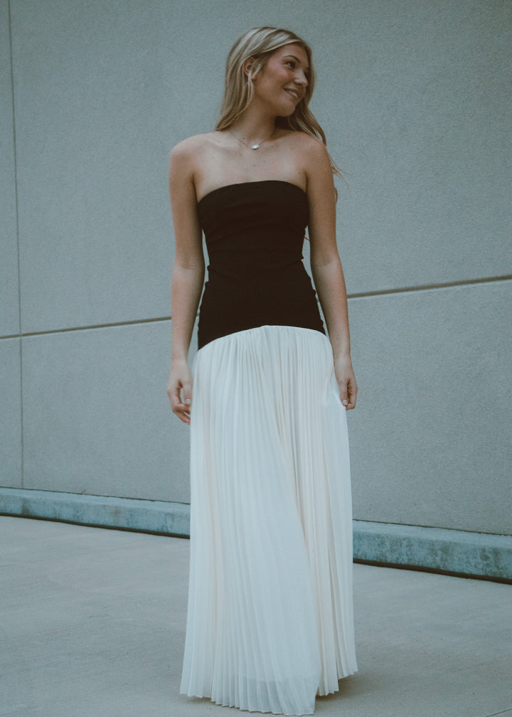 Woman wearing a black and white strapless pleated dress against a gray wall.