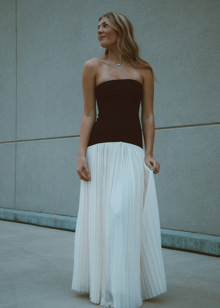 Woman wearing a strapless black and white pleated dress against a neutral wall.
