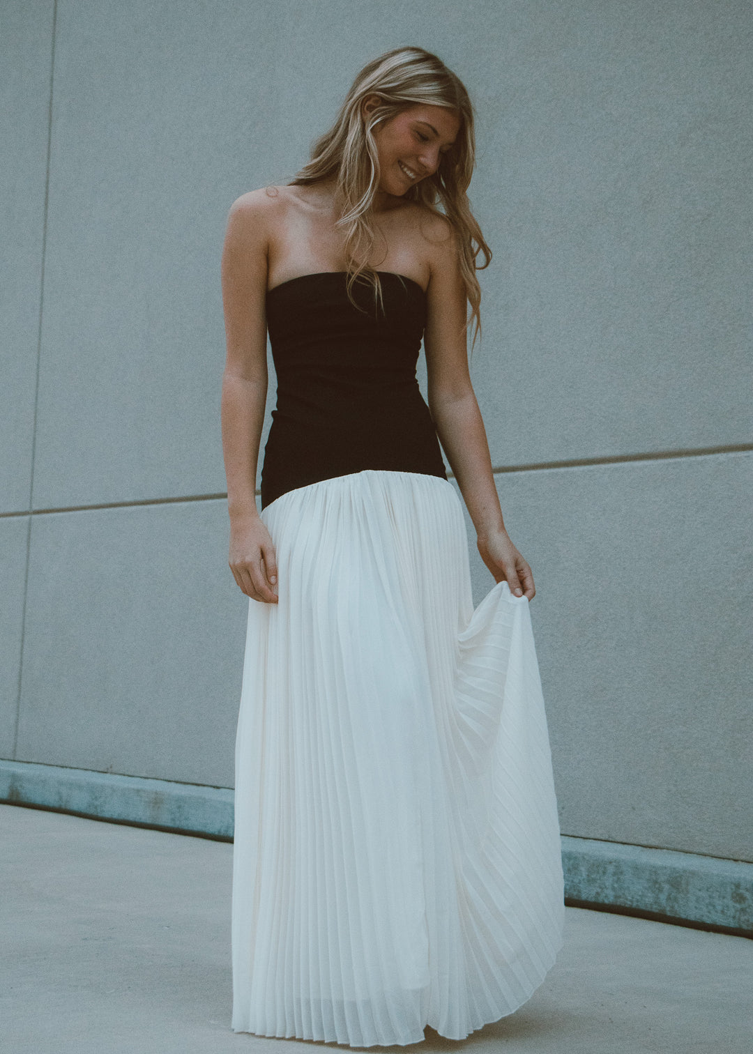 Woman wearing a black and white pleated dress against a light gray wall.