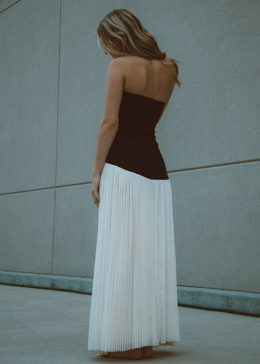 Woman wearing a black and white pleated dress against a light blue wall.