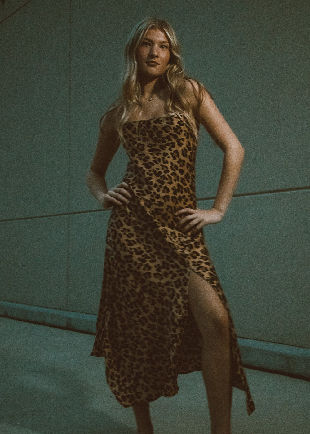 Woman wearing a leopard print dress with a slit, standing against a plain background