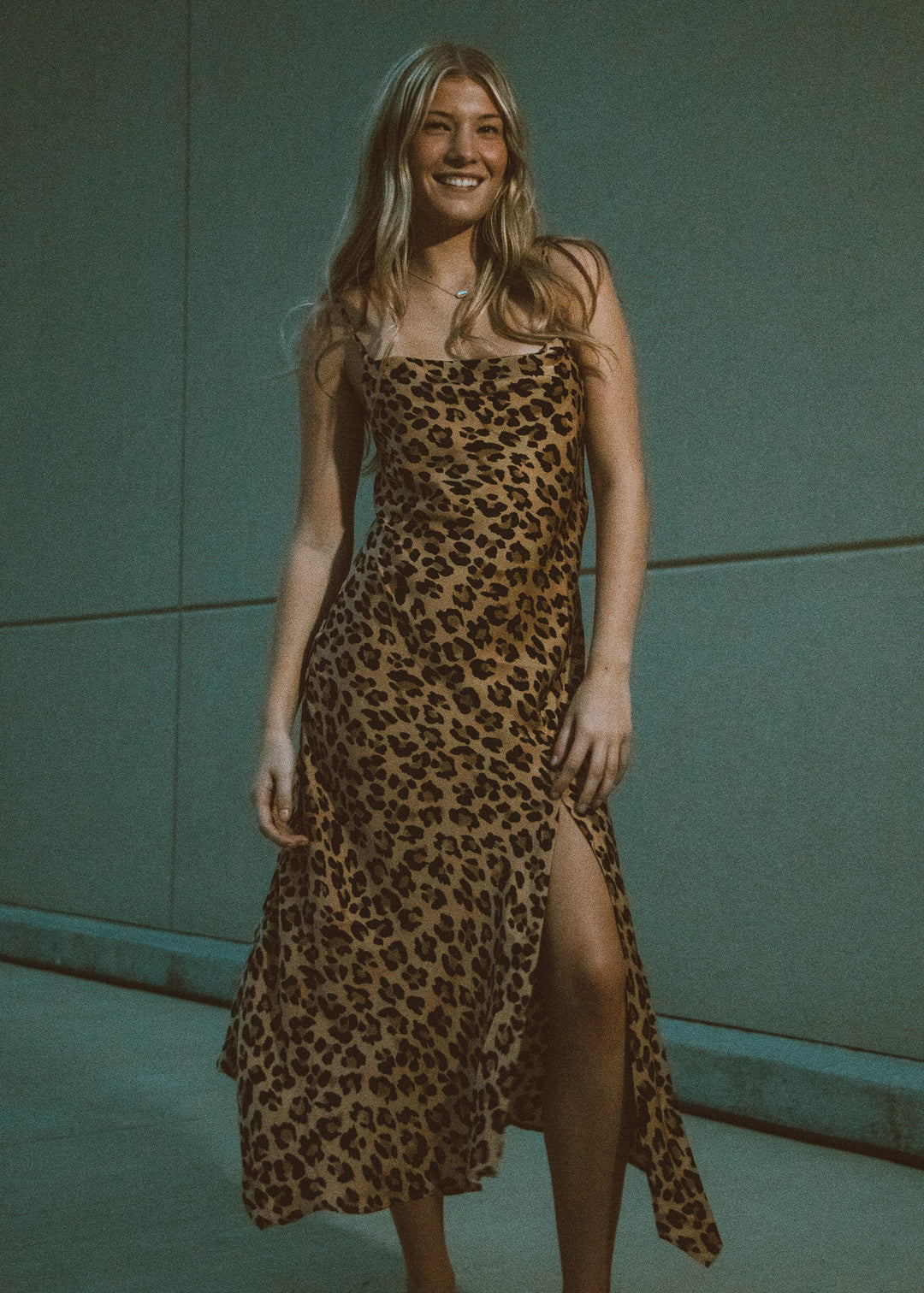 Woman wearing a leopard print dress against a tan wall.