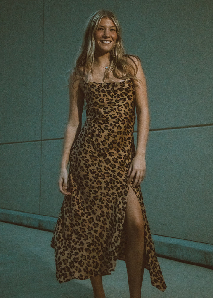 Woman wearing a leopard print dress against a tan wall.