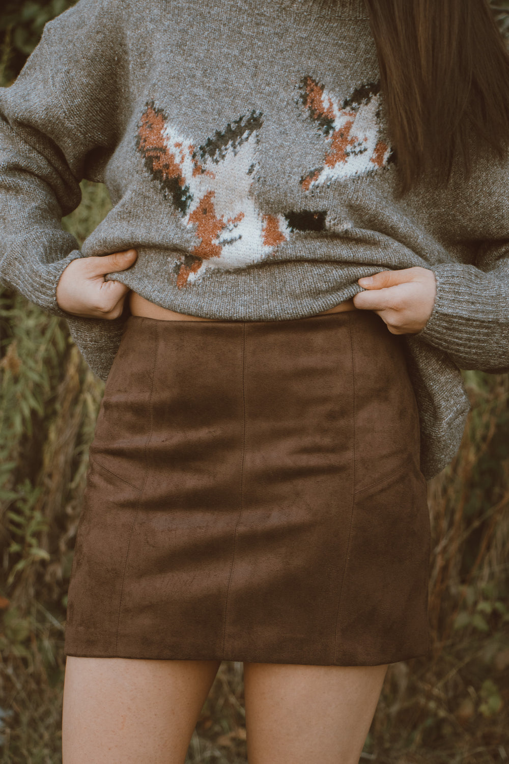 Person wearing a sweater with a duck design and a brown skirt outdoors.