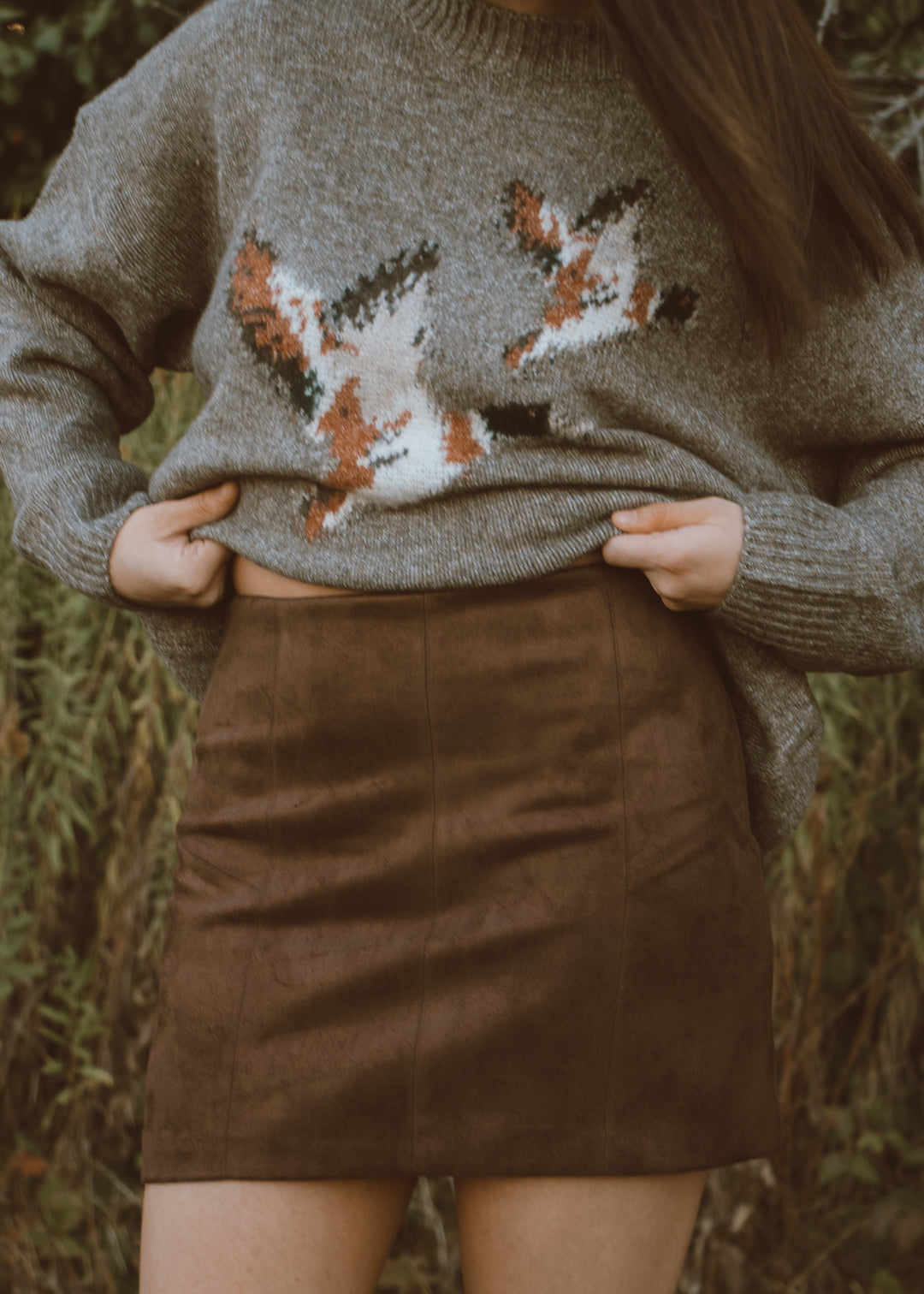 Person wearing a sweater with duck design and a brown skirt outdoors