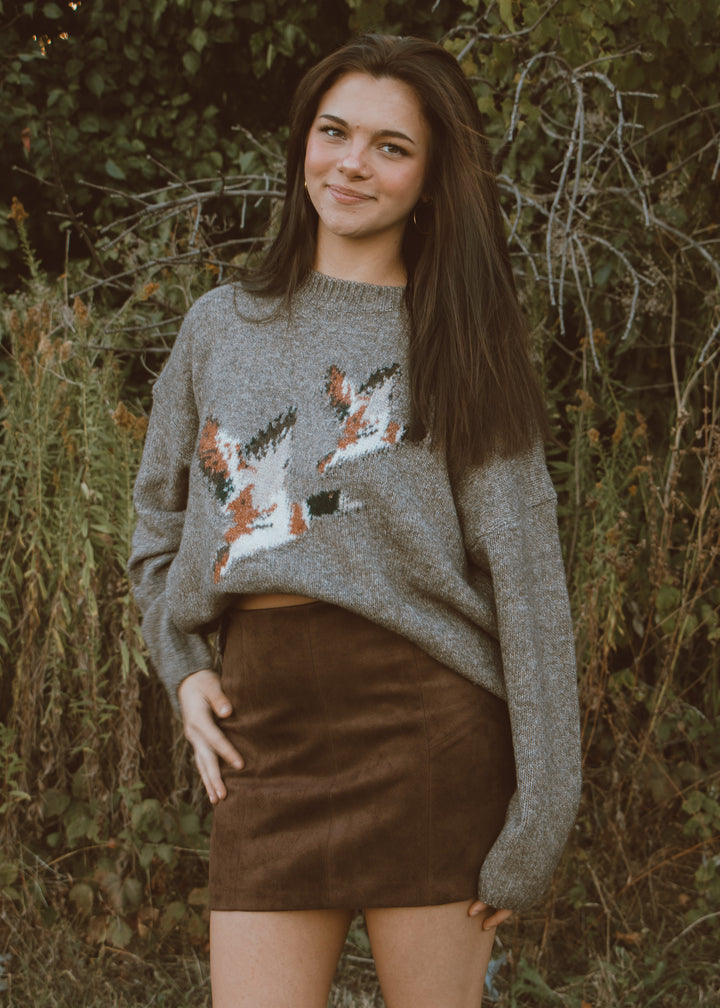 Woman wearing a patterned sweater and brown skirt standing in a natural setting