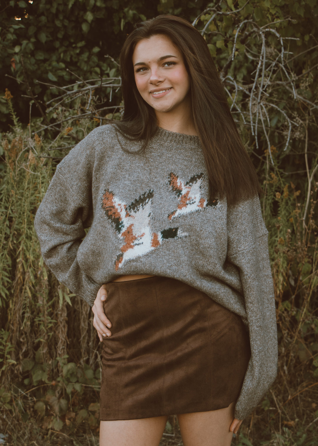Woman wearing a gray sweater with duck patterns in a natural setting