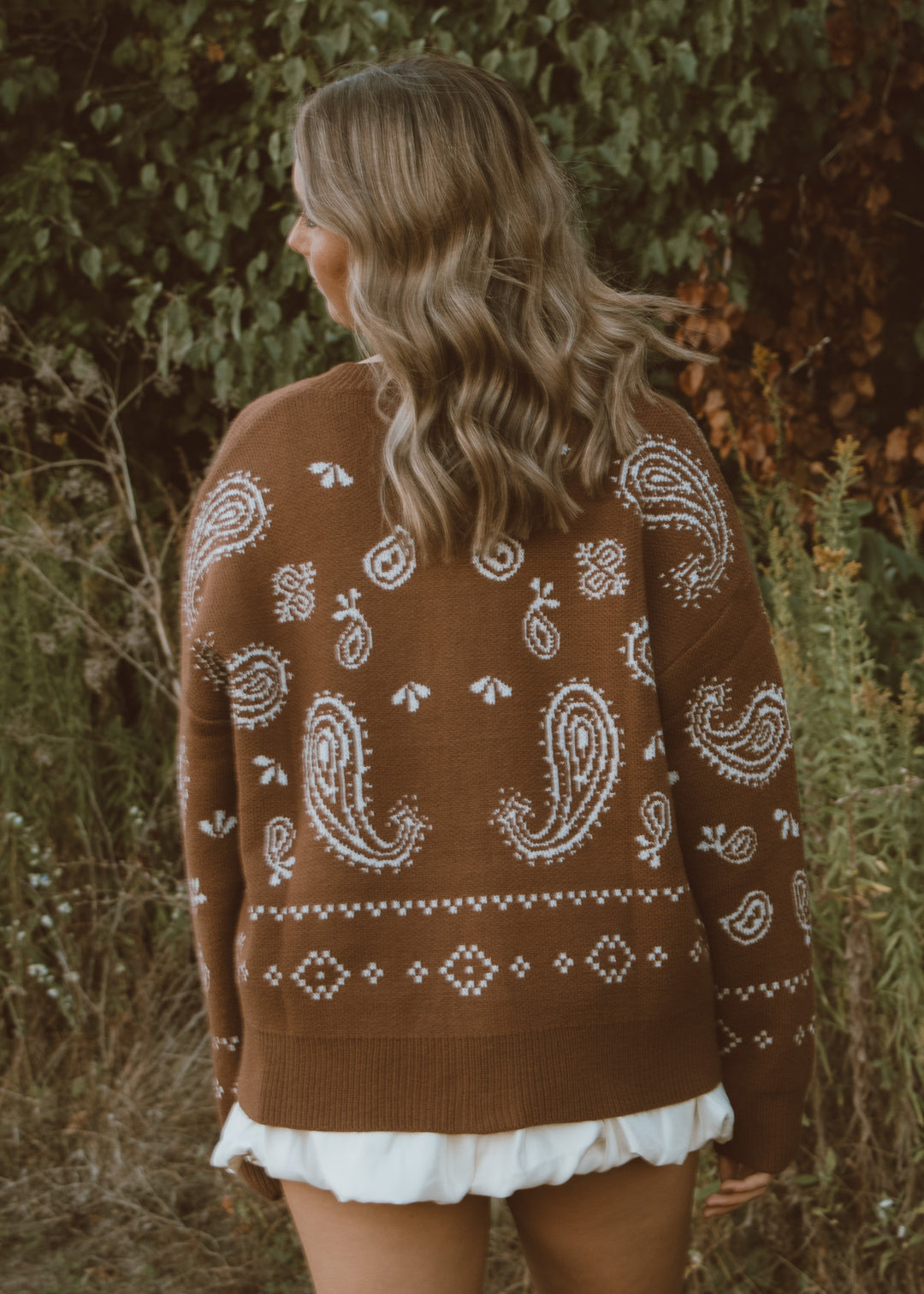 Person wearing a brown sweater with white paisley patterns in a natural setting.
