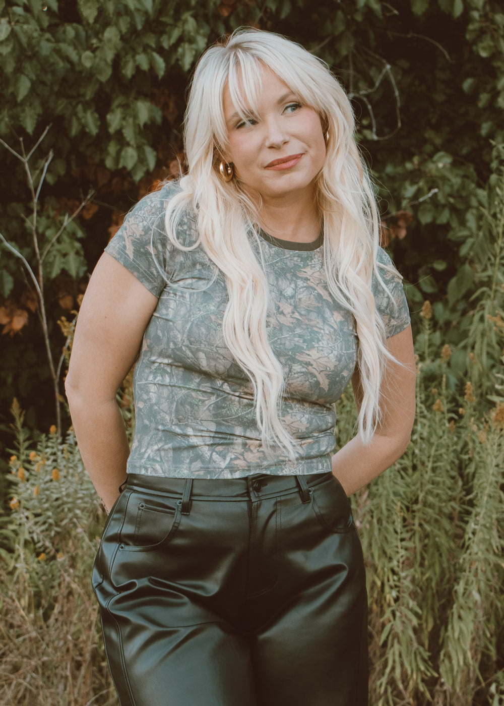 Woman in camo baby-tee and black leather pants.