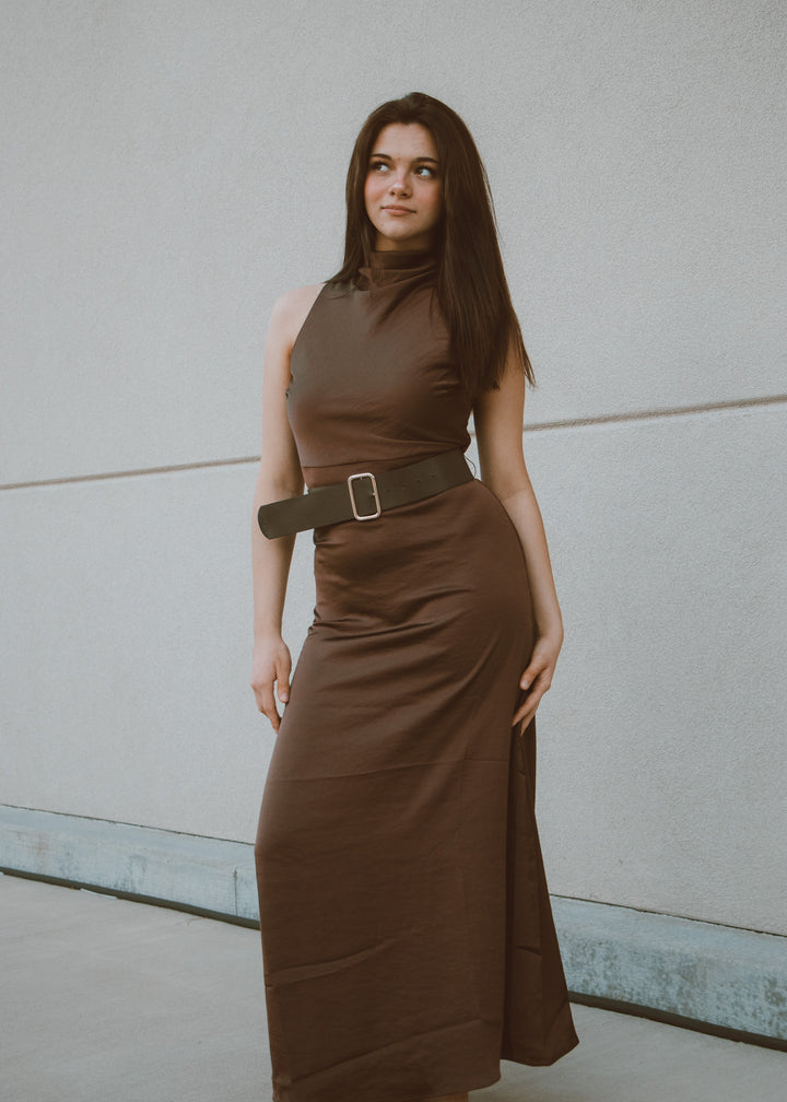 Woman wearing a brown dress with a belt against a plain background