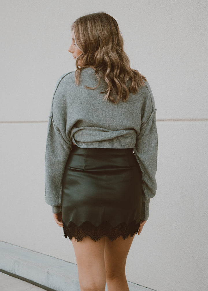 Person wearing a grey sweater and black skirt against a light background