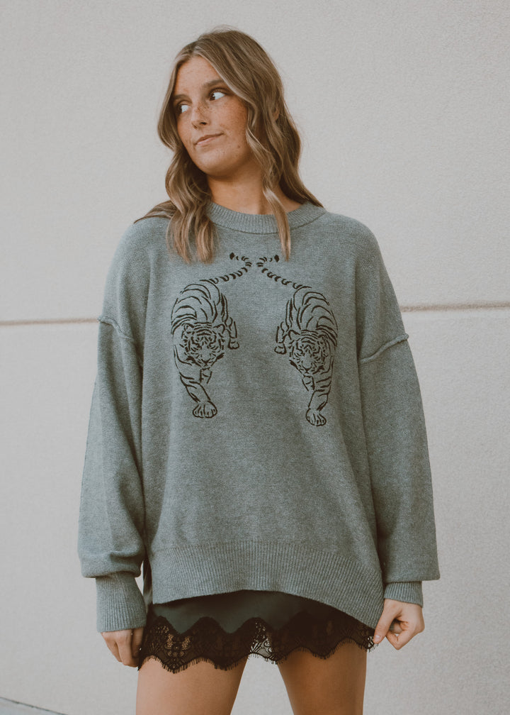 Woman wearing a gray sweater with tiger designs against a plain background