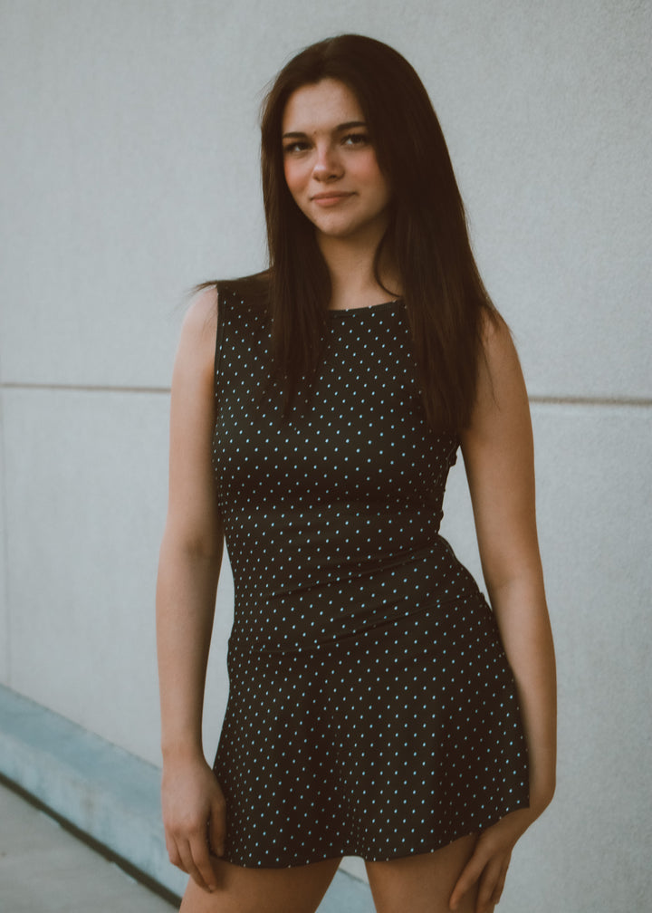Woman wearing a black polka dot dress against a plain background