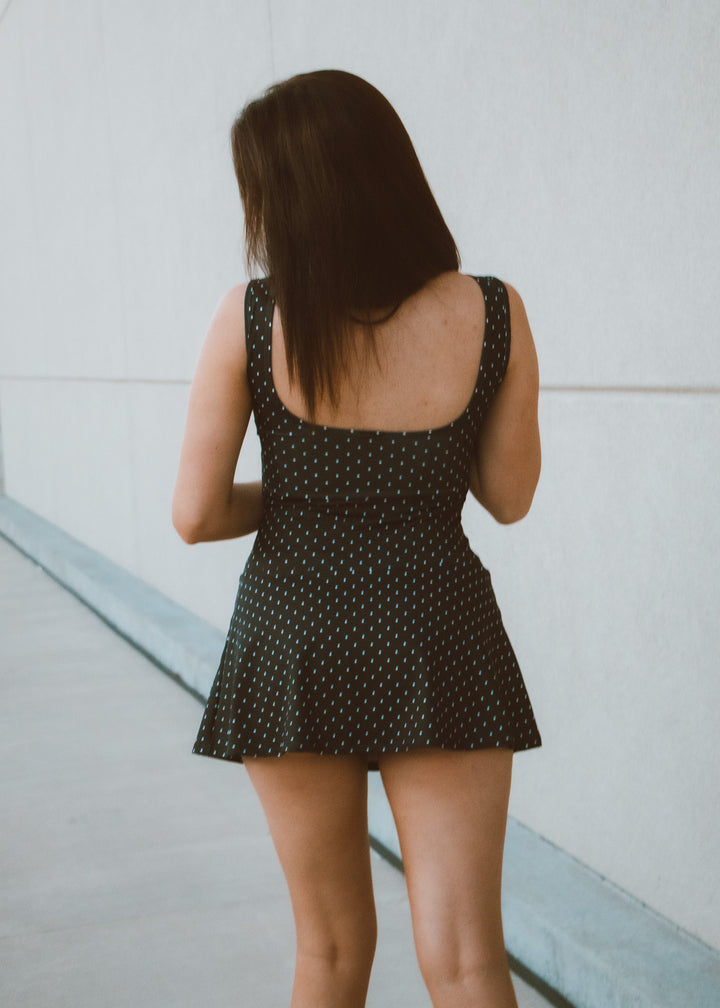Woman wearing a black polka dot dress against a light gray wall.