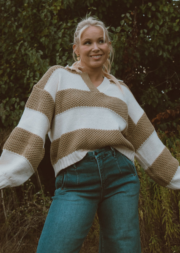 Woman wearing a green and white striped sweater and blue jeans standing outdoors.
