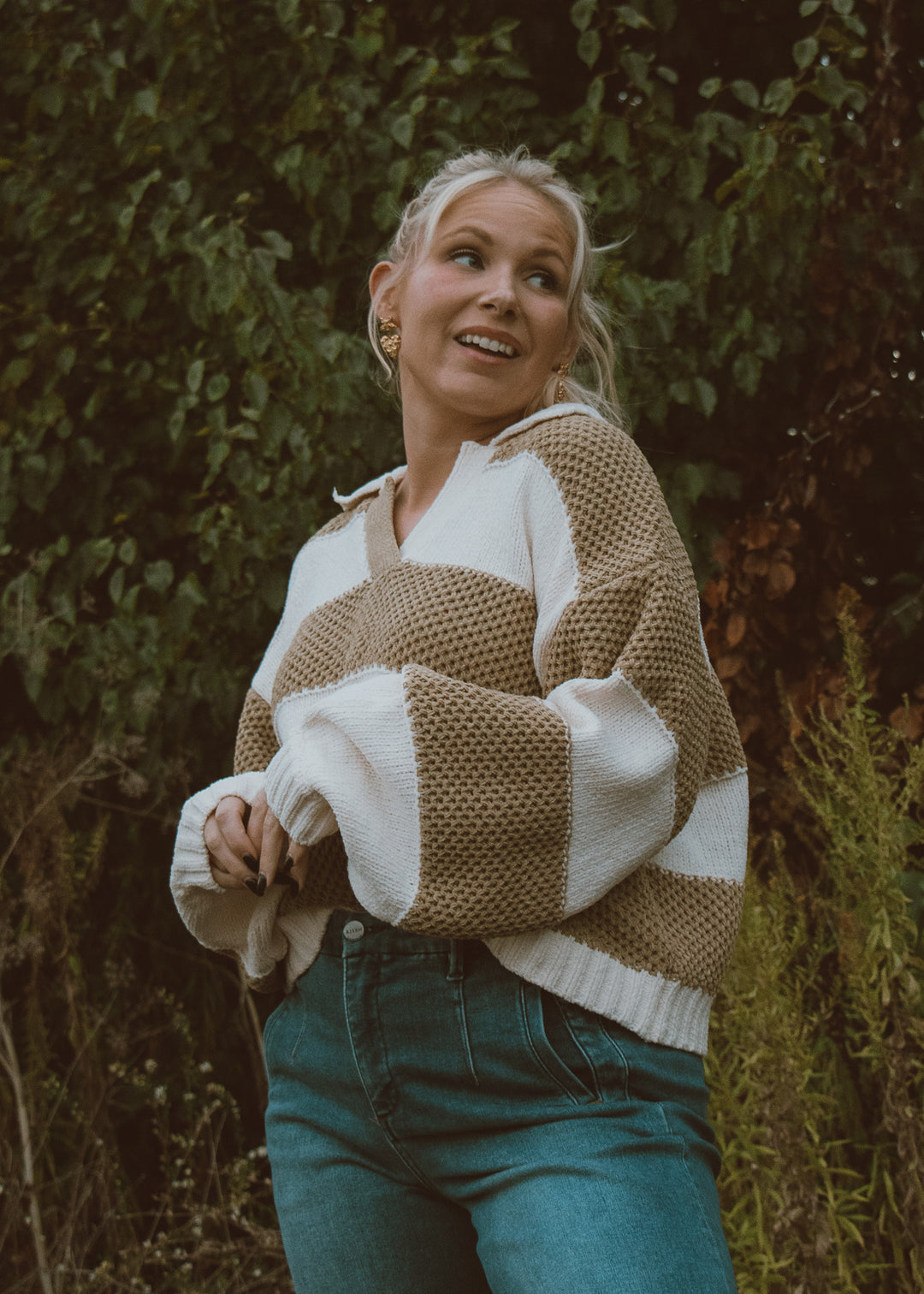 Woman wearing a patterned sweater and jeans standing in a natural setting