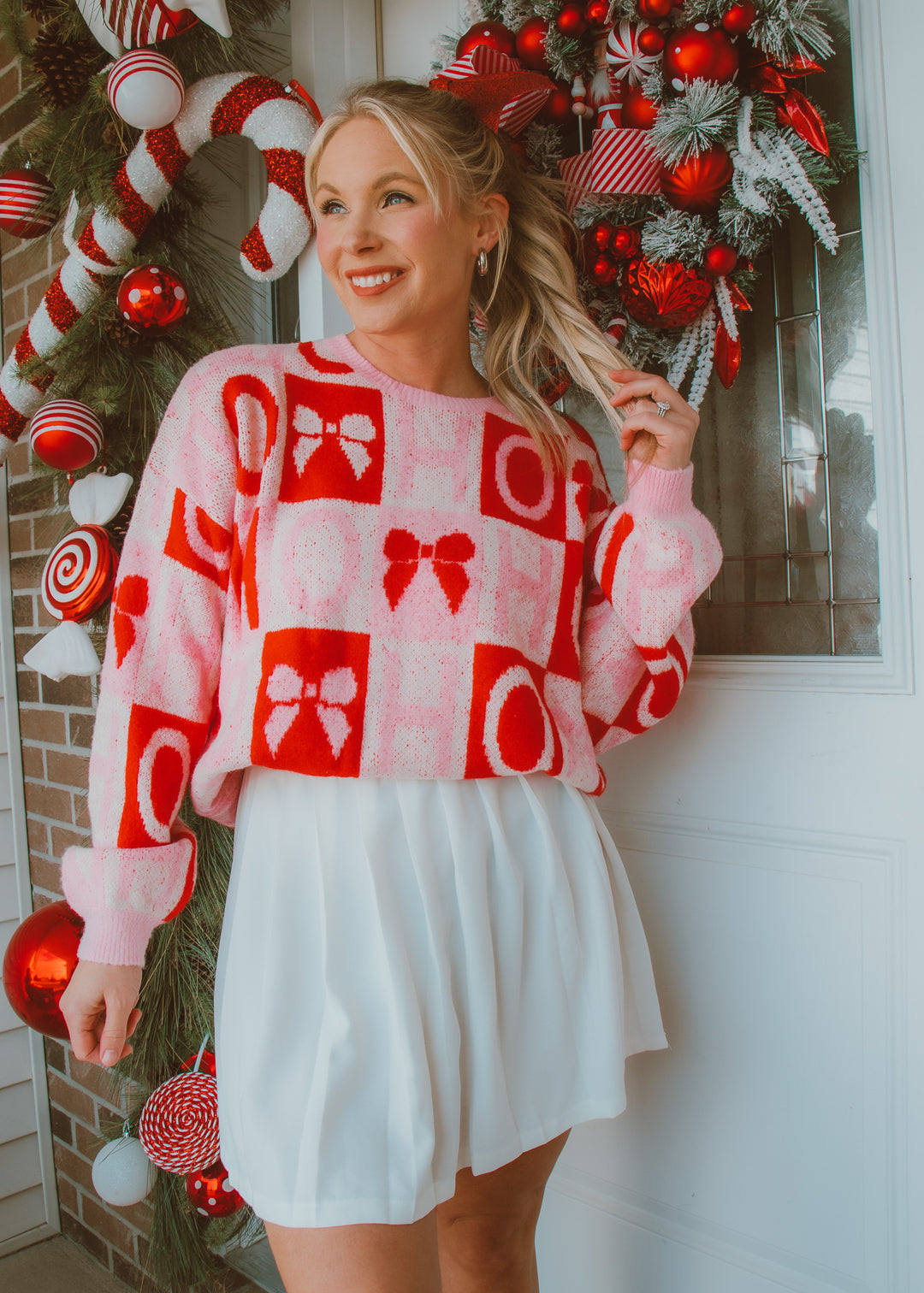 Woman wearing a festive sweater with red and white patterns in front of a decorated Christmas wreath.