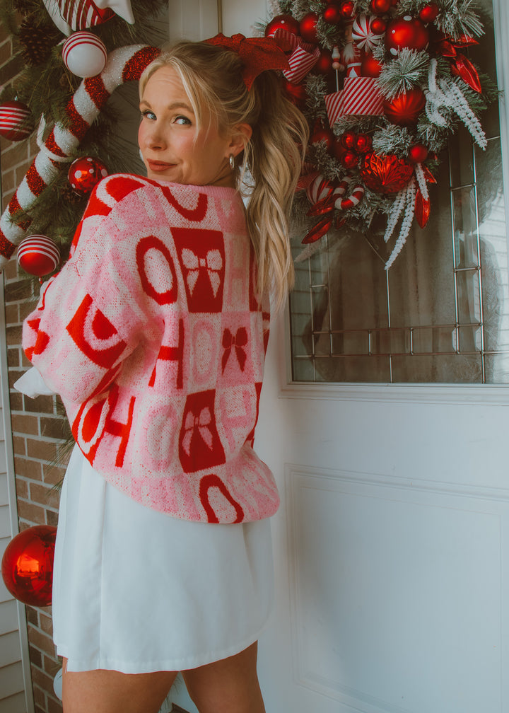 Woman wearing a red and white patterned holiday sweater in front of a decorated Christmas wreath