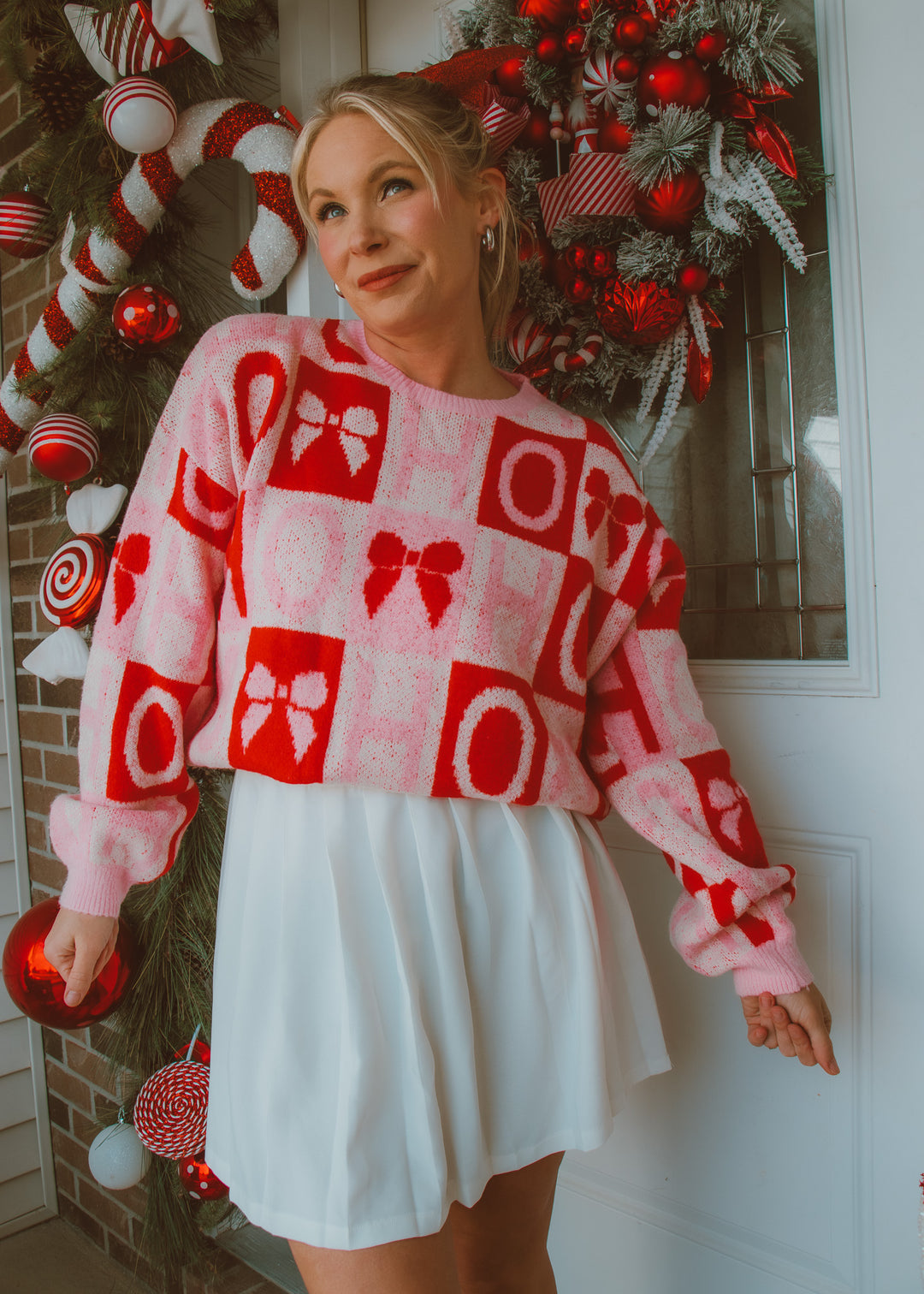 Woman wearing a red, pink and white patterned sweater in front of a decorated Christmas wreath.