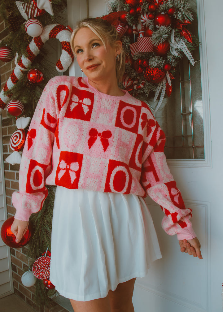 Woman wearing a red, pink and white patterned sweater in front of a decorated Christmas wreath.