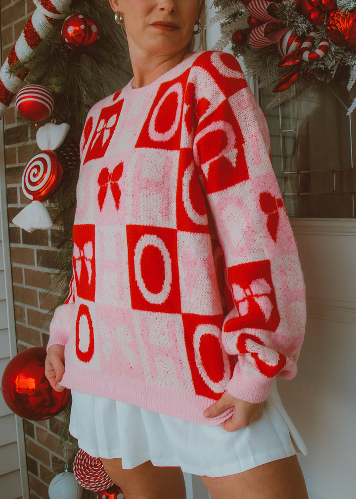 Person wearing a red and white patterned holiday sweater with bows  and Christmas decorations in the background
