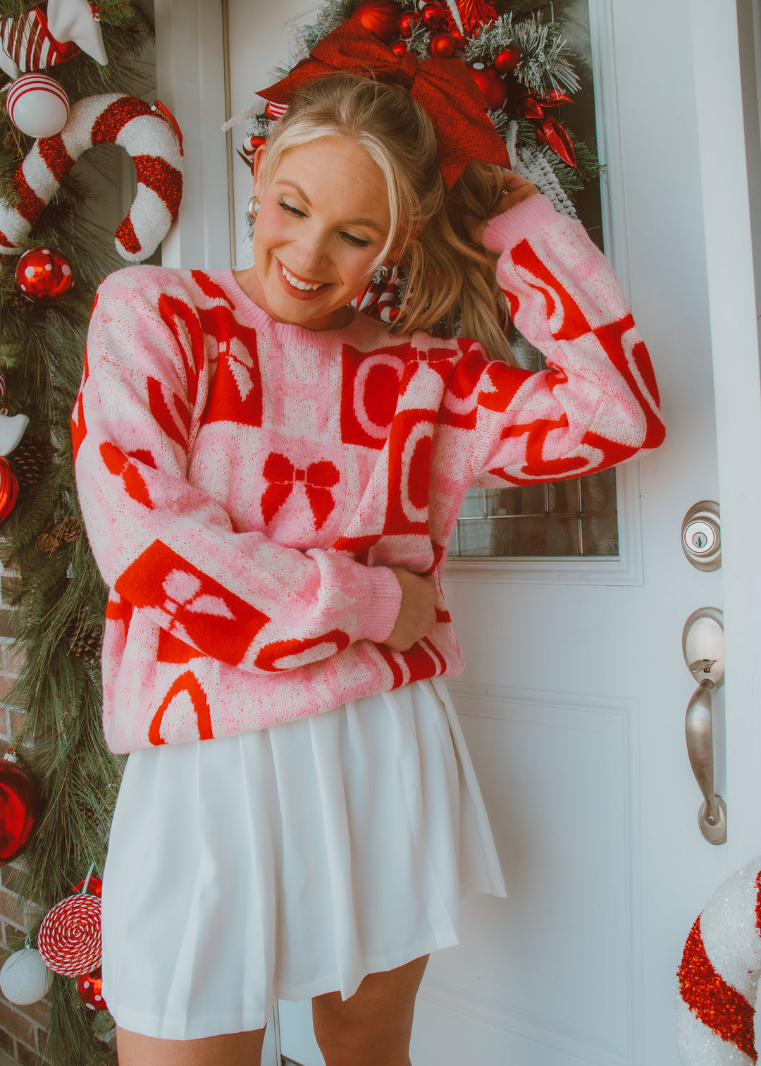 Person wearing a red and white patterned sweater with bows in front of a decorated door.