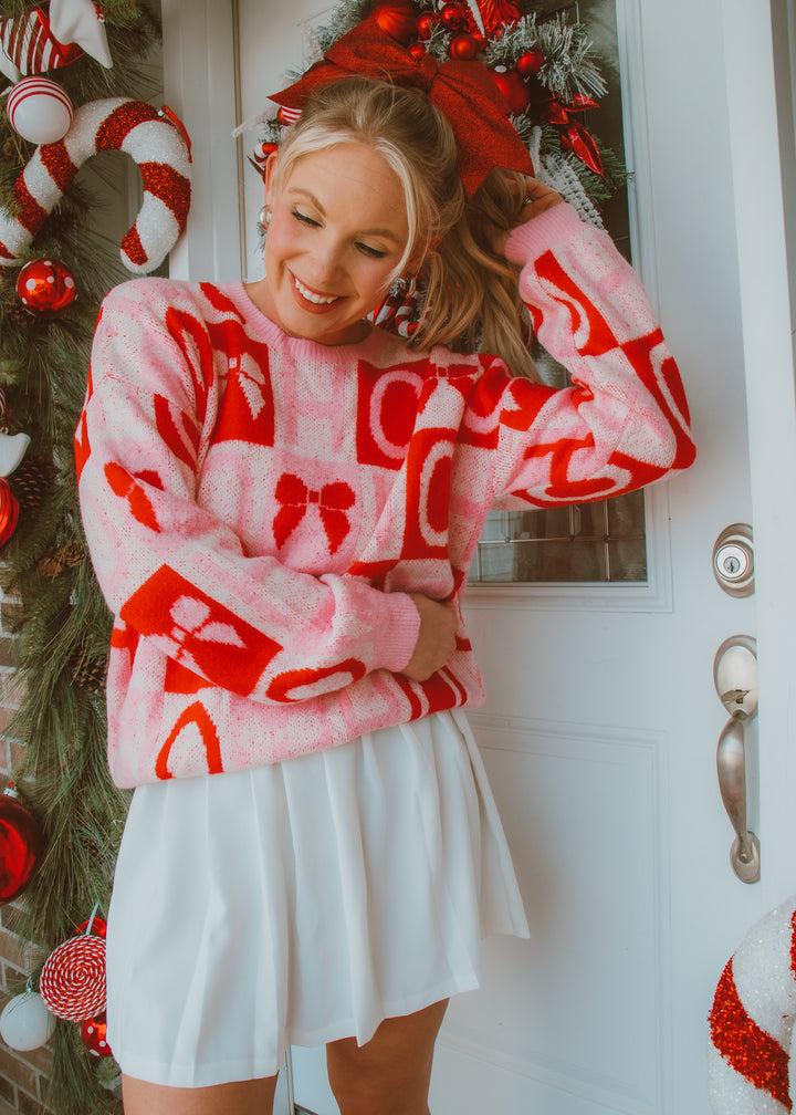 Person wearing a red and white patterned sweater with bows in front of a decorated door.