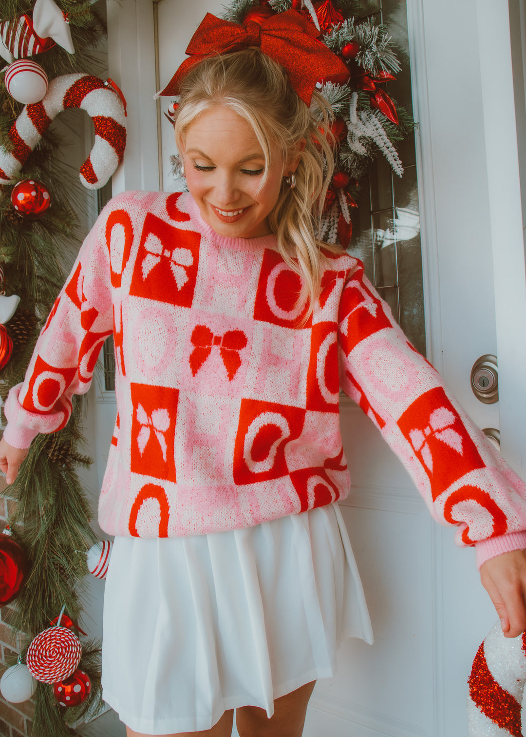 Woman wearing a festive sweater with red bows in a Christmas-themed setting