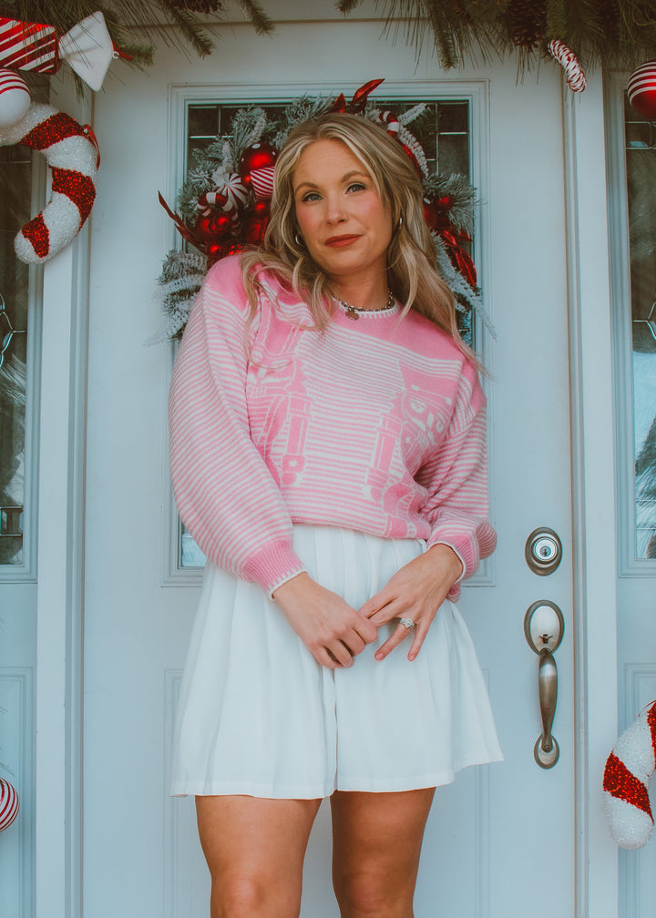 Woman in a pink and white striped sweater and white skirt standing in front of a decorated door with Christmas decorations.