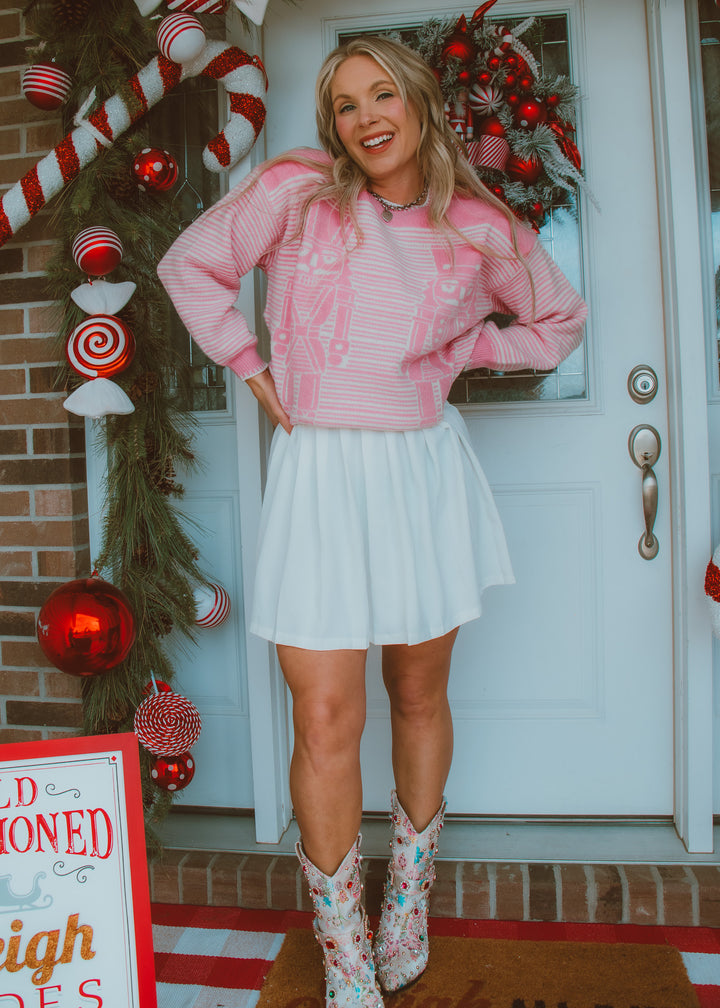 Woman in pink sweater and white skirt standing in front of a decorated door with Christmas decorations.