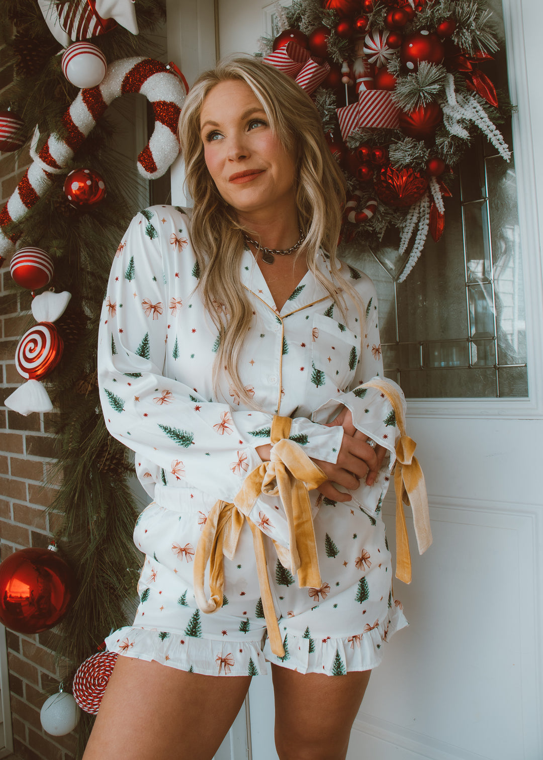 Woman in a festive pajama set standing in front of a decorated door with Christmas decorations.