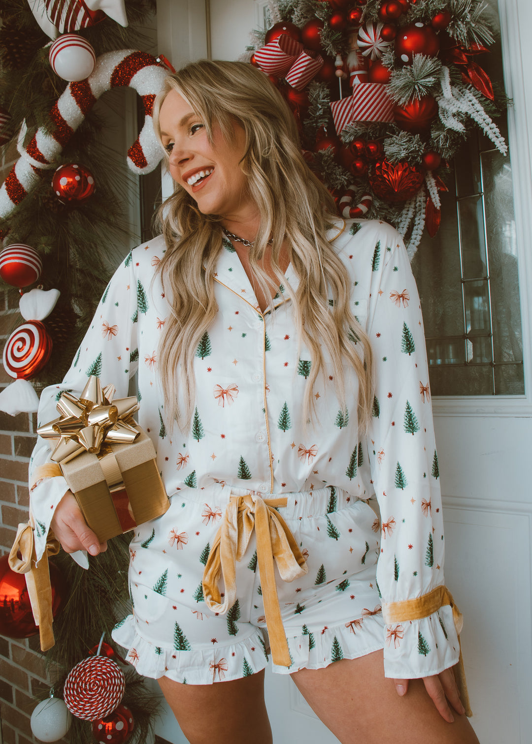 Woman in festive pajama set holding a gift, surrounded by Christmas decorations.