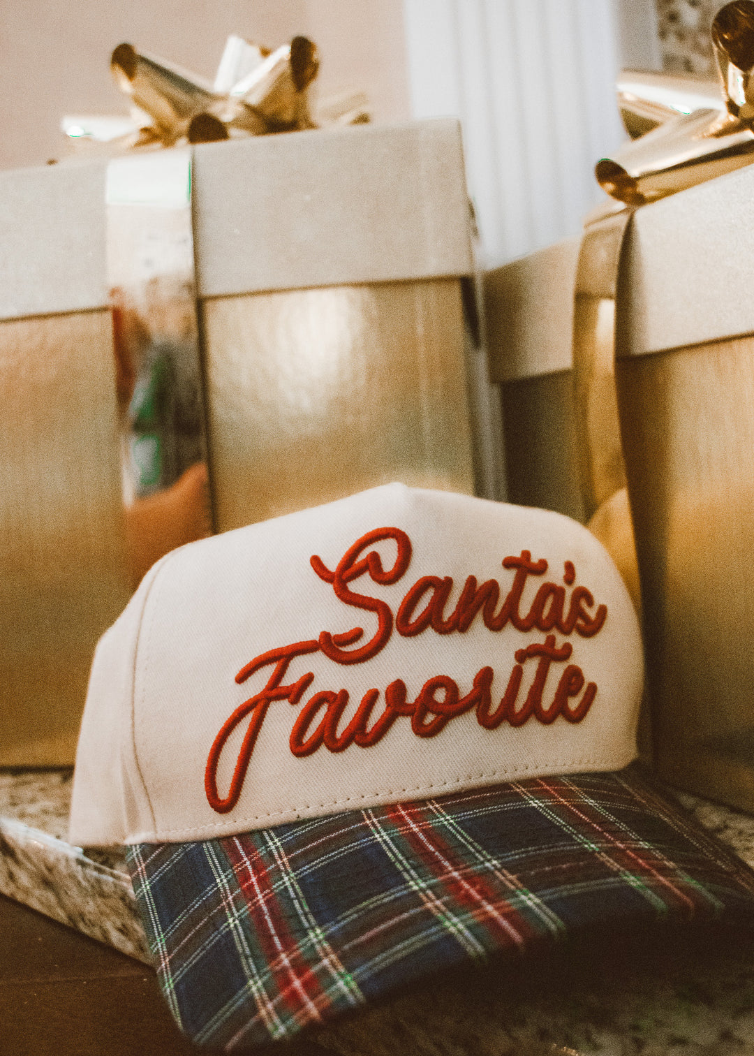 Cap with 'Santa's Favorite' text on a plaid surface with gift boxes in the background