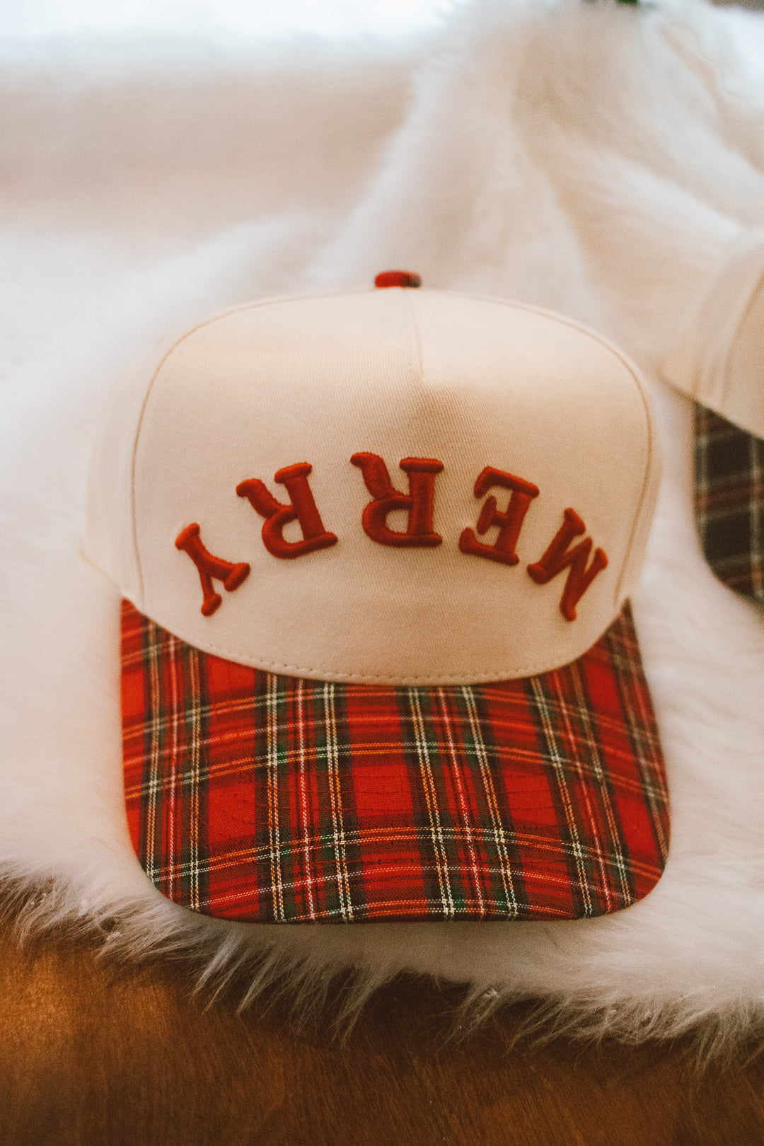 Cap with plaid brim and 'MERRY' embroidery on a fluffy white surface