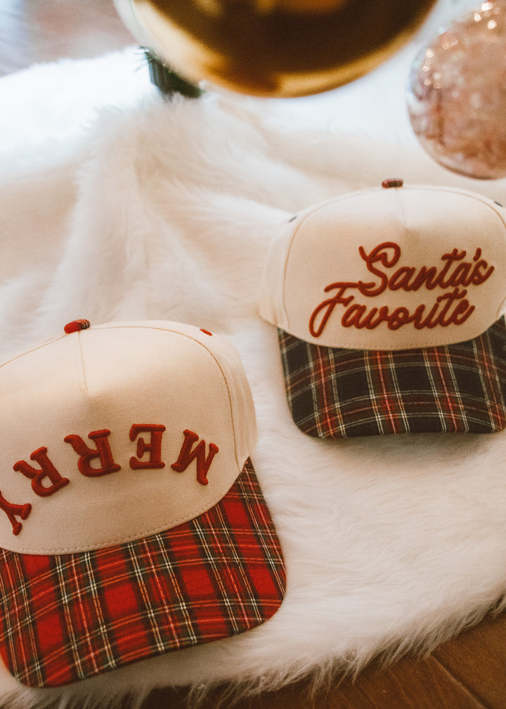 Two Christmas-themed hats with plaid patterns and embroidered text on a fur surface.
