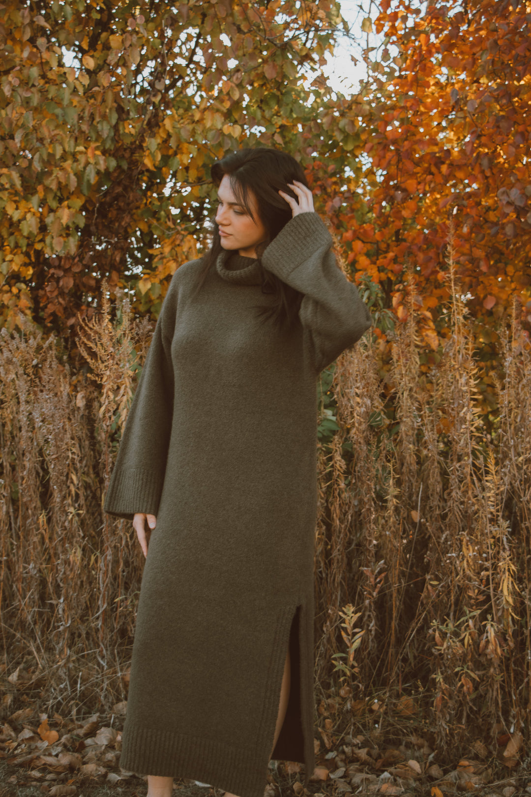 Woman in a long green turtleneck dress standing in an autumn forest