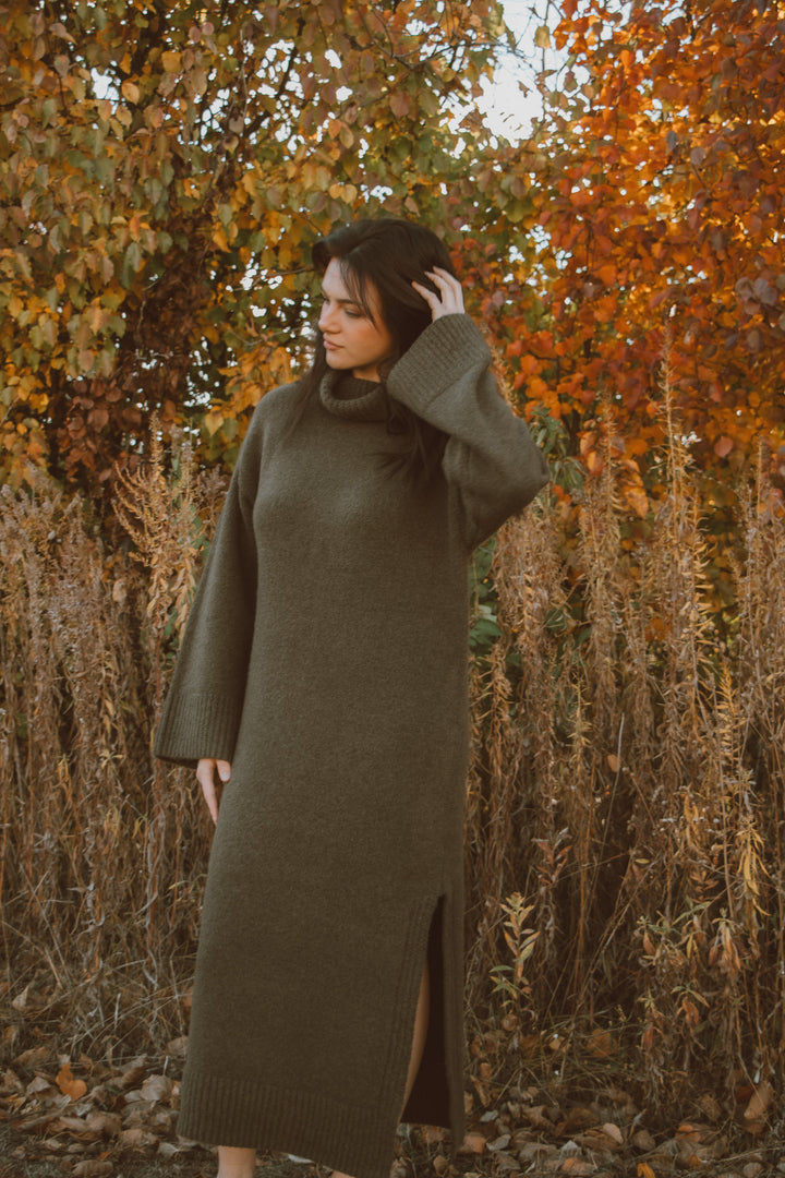 Woman in a long green turtleneck dress standing in an autumn forest