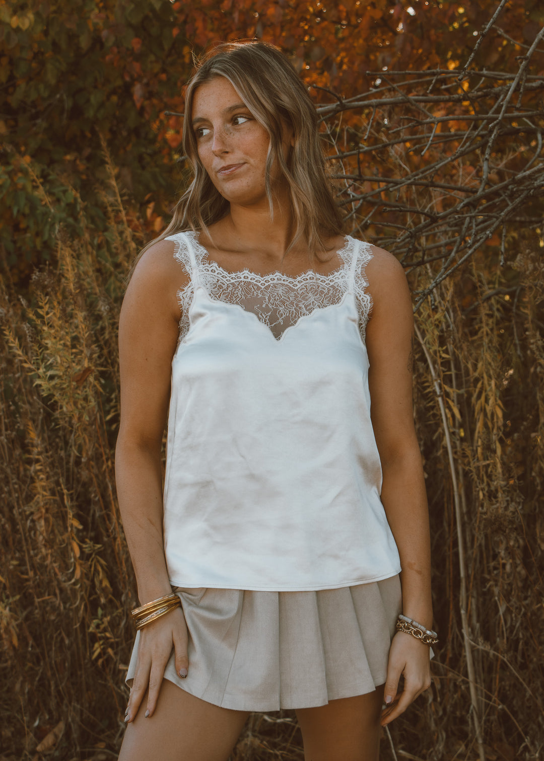 Woman wearing a white lace top and a beige skirt standing against a natural background
