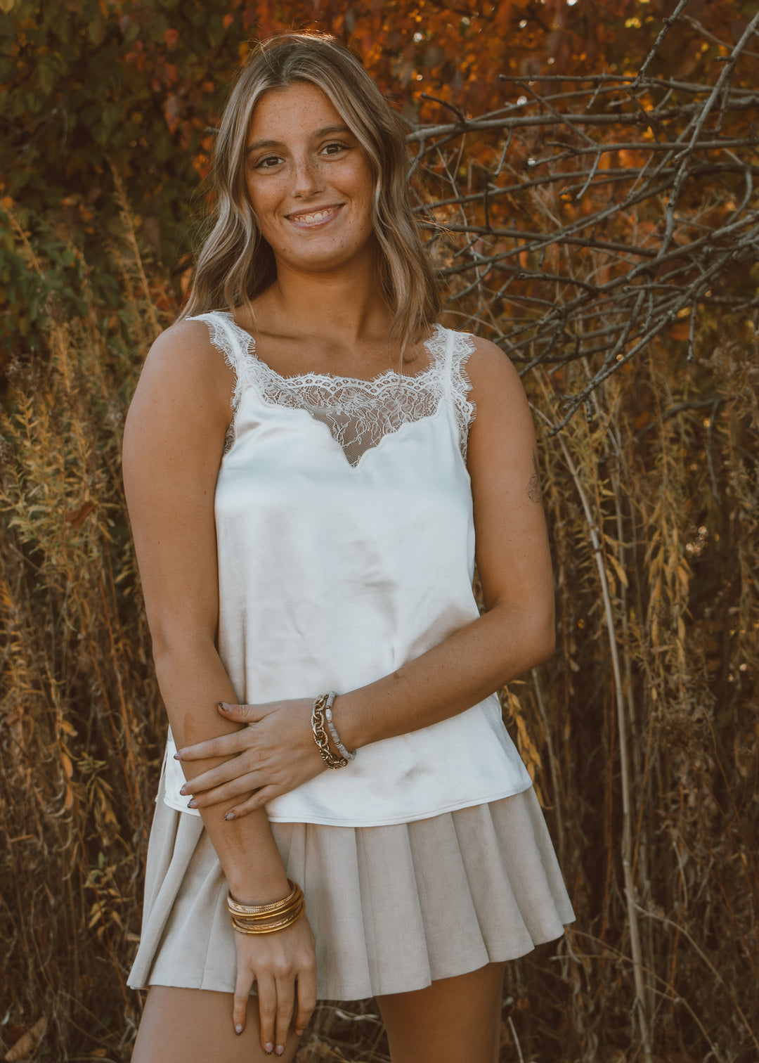 Woman wearing a white lace top and beige skirt standing against a natural background