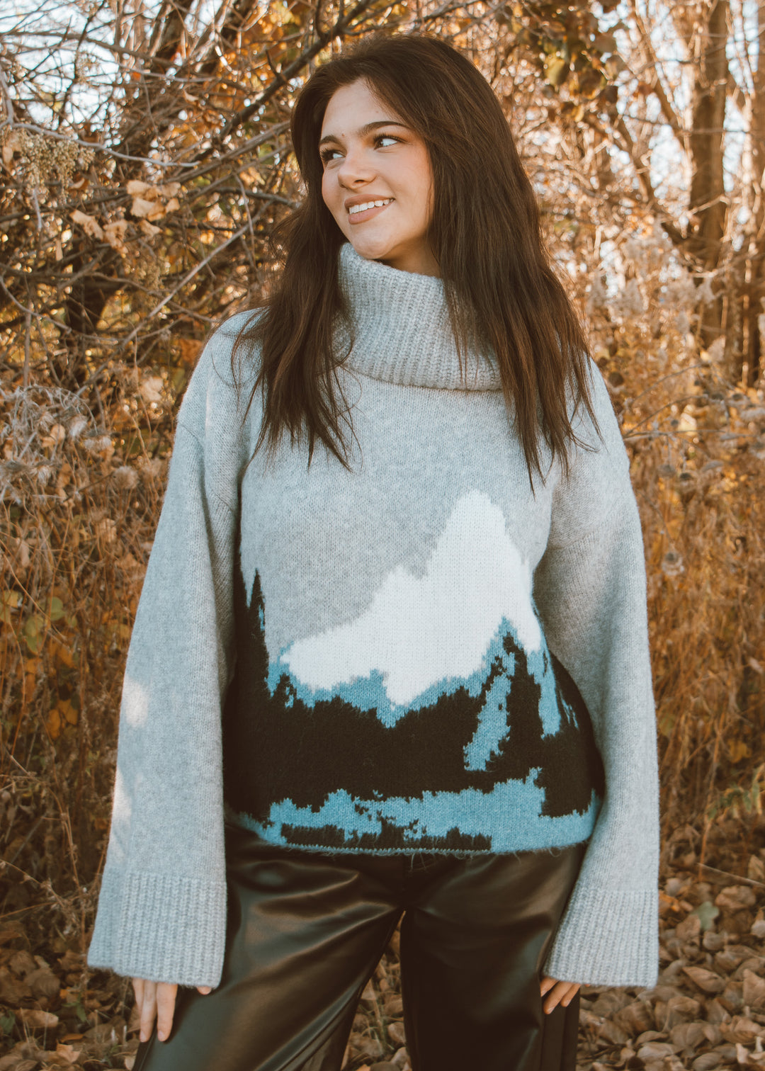 Woman wearing a sweater with a mountain design in a forest setting