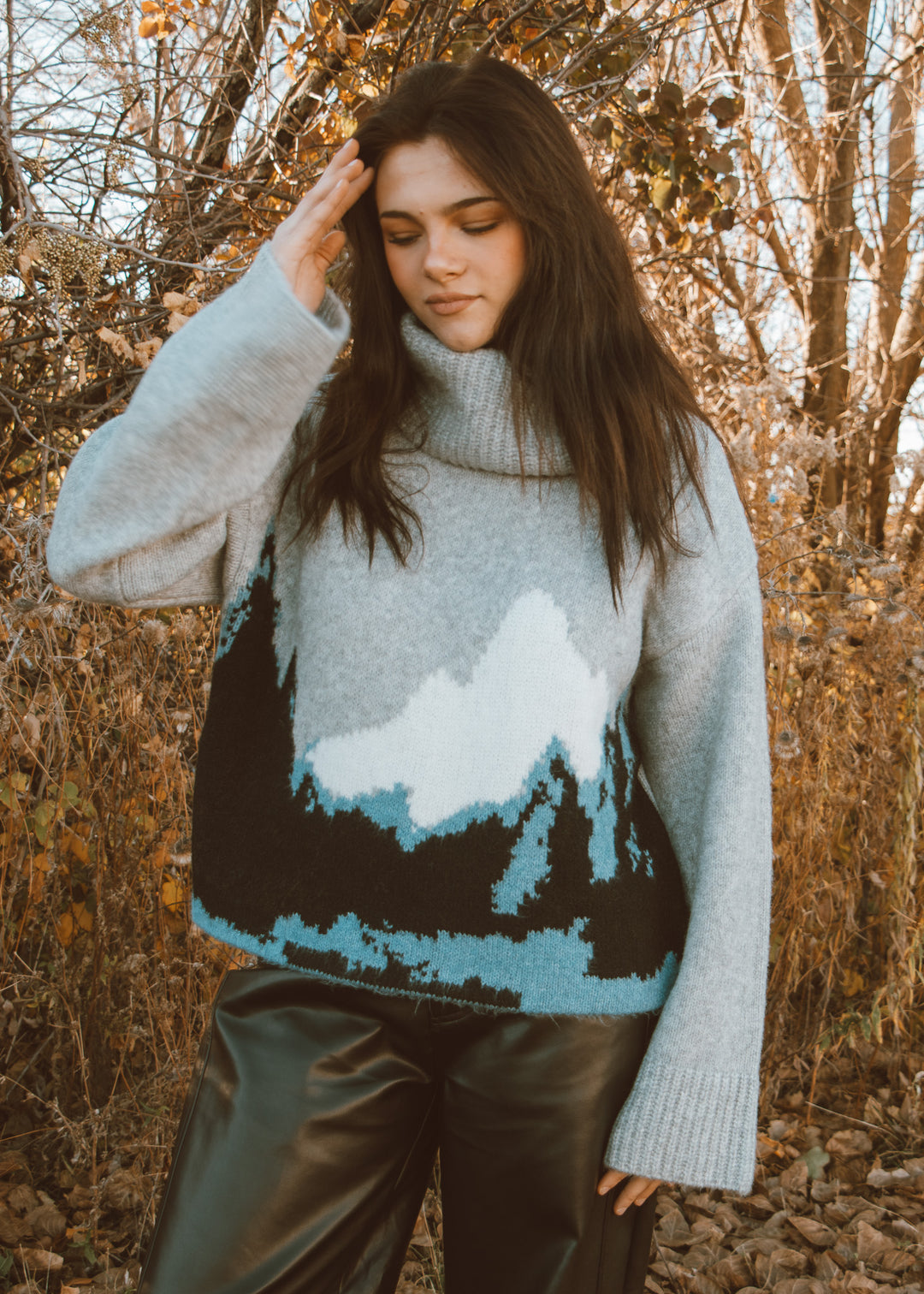 Woman wearing a sweater with a mountain design in a forest setting