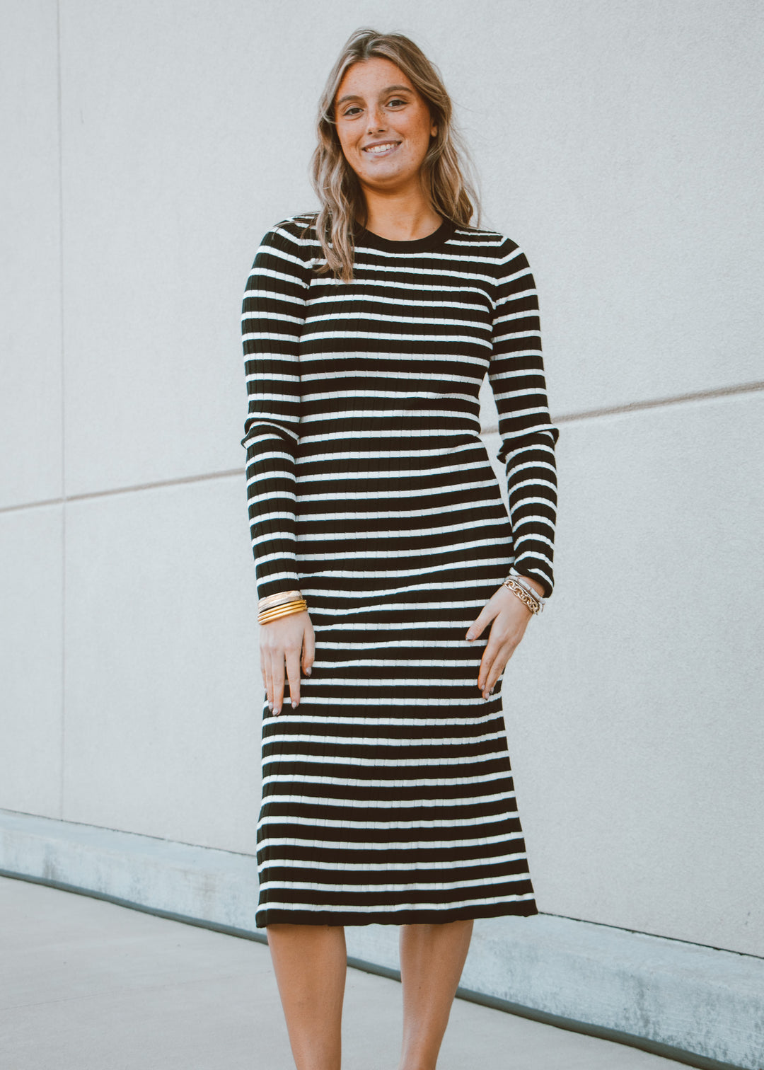 Woman wearing a black and white striped dress standing against a light gray wall.