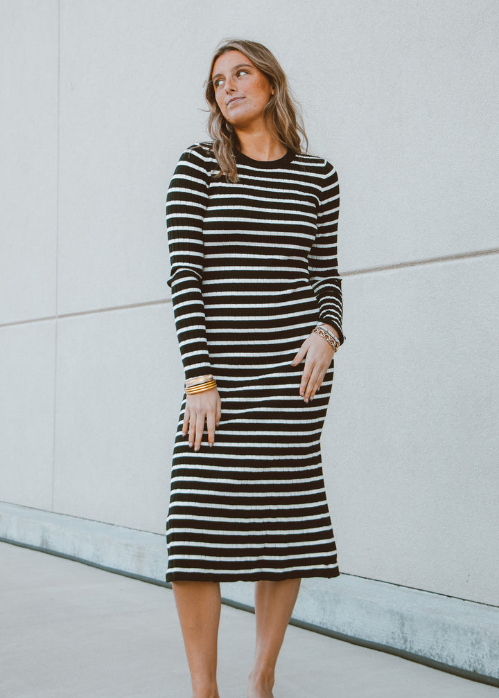 Woman wearing a black and white striped dress against a light gray wall.