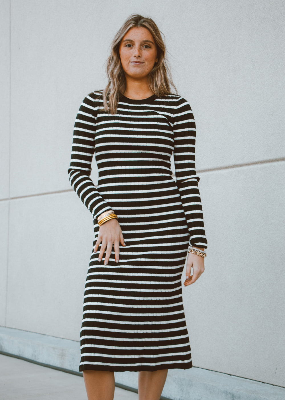 Woman wearing a black and white striped dress against a light gray wall.