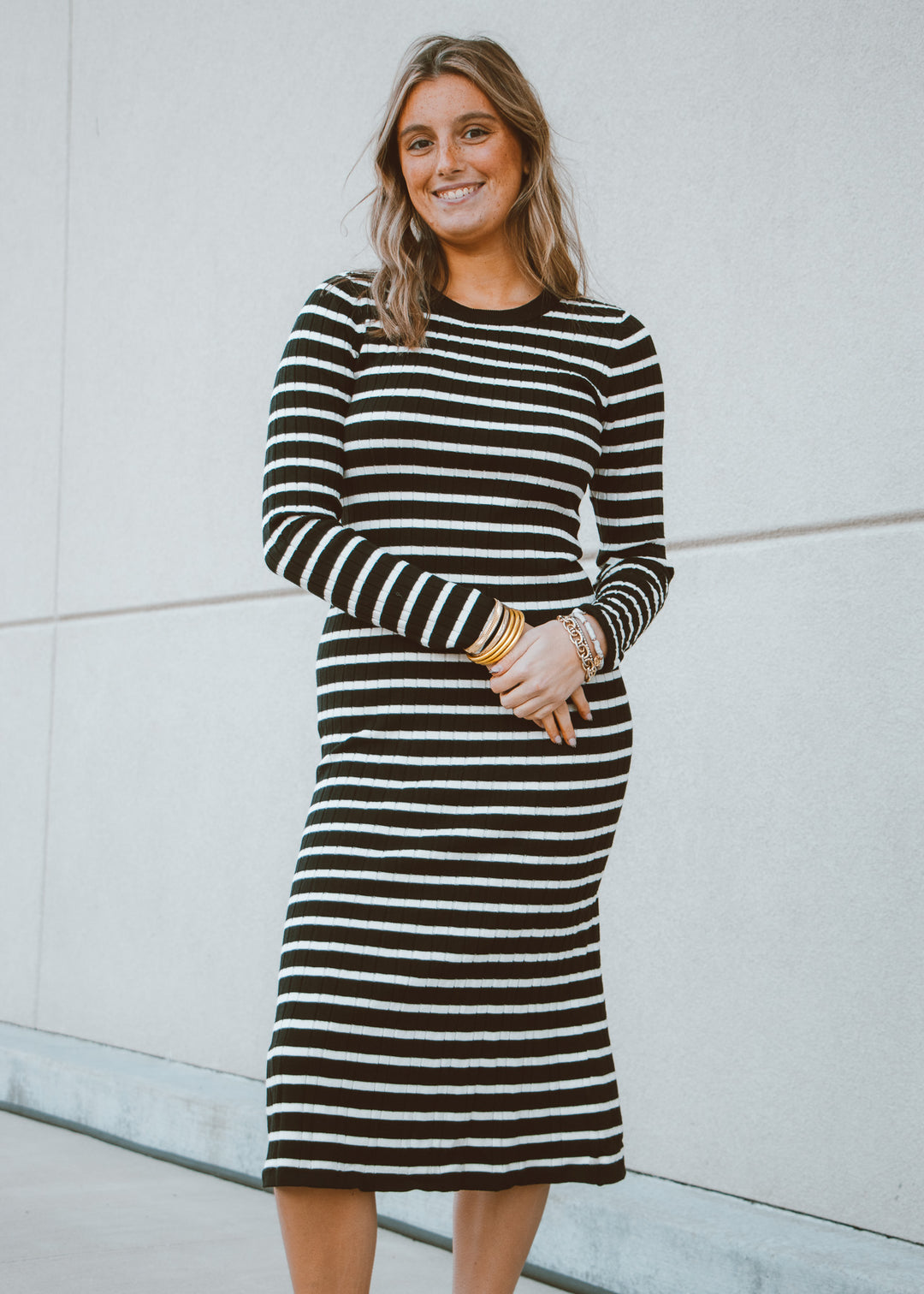 Woman wearing a black and white striped dress standing against a light gray wall.
