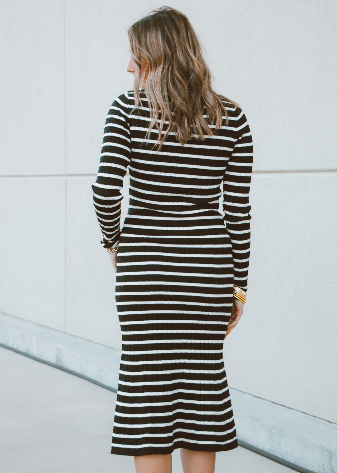 Woman wearing a black and white striped dress against a light-colored wall.
